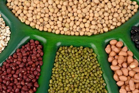 Grains such as soybeans, green beans, red beans, black beans, millet and peanuts on wooden trays.