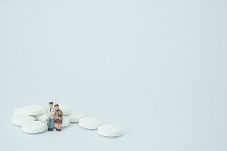 Elderly couple figure sitting on a pile of white pills.の写真素材