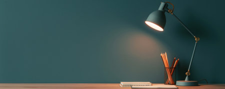 A modern workspace showcasing a stylish lamp, wooden desk, and stationary elements against a deep teal wall.の素材