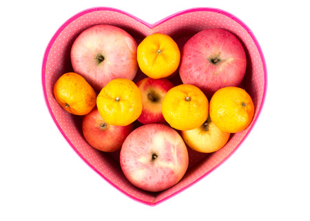 orange and apple mixed in heart-shaped gift box on whiteの写真素材