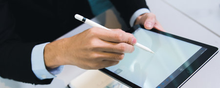 business person holding digital tablet and working with computer, occupation of internet communication technology working in modern indoors office, using hand to touch screen close-upの写真素材