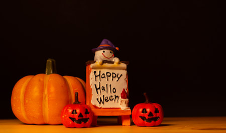 Halloween pumpkins with painted faces and ghost dolls on old wood desk, black background and copy space for textの写真素材
