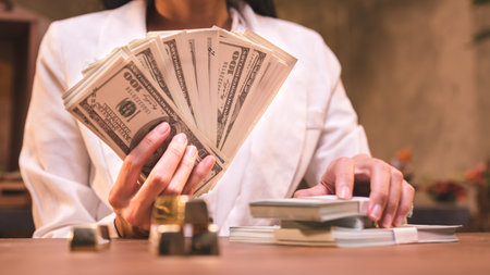 Successful businesswoman holding a large amount of money and gold bars on the table in the officeの写真素材
