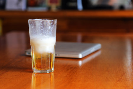Half of beer in glass after drink on wooden table have laptop in background in the bar.の写真素材
