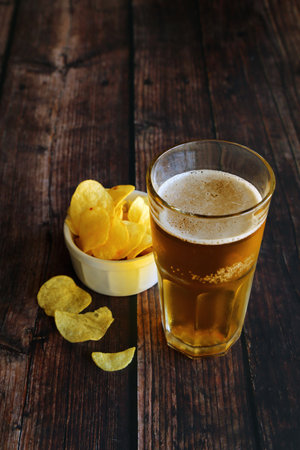 A glass of light foamy beer with potato chips on a wooden table and have copy space.の写真素材