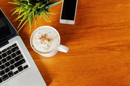 Hot Latte on wooden table in cafe with laptop and smartphone have blank space for any wording. Hot Chocolate on desk have computer notebook and mobile phone background.の写真素材