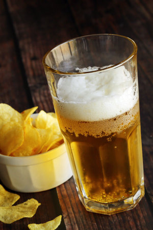 Light foamy beer with potato chips on a wooden table.の写真素材