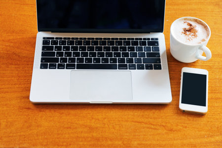 Laptop with smartphone and hot coffee on wooden table, Working remotely.