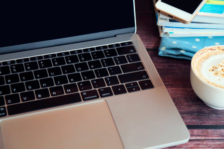 Laptop with a cup of hot coffee, smartphone and magazine on wooden table, Working remotely.