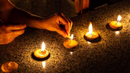 Close up shot of hands of a woman who is lighting five Thai styled candles called Pangpratis or Pangpratheep made from clay, wax and cotton during Loy Krathong or Yeepeng festival in Chiang Mai, Thailandの写真素材