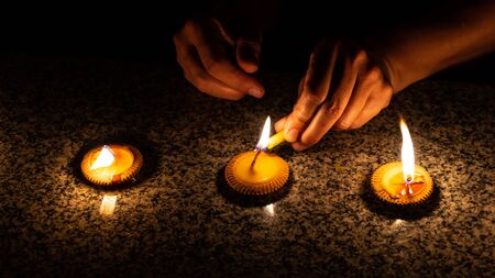Close up shot of hands of a woman who is lighting three Thai styled candles called Pangpratis or Pangpratheep made from clay, wax and cotton during Loy Krathong or Yeepeng festival in Chiang Mai, Thailandの写真素材