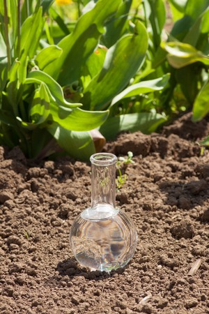 flask with clear water or fertilizer on dry soilの写真素材