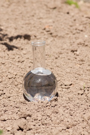 flask with clear water or fertilizer on dry soilの写真素材