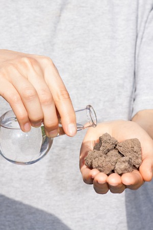 dry soil in female hand and a flask with waterの写真素材
