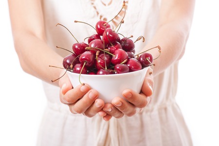 bowl of cherries in women's hands, isolated on white の写真素材