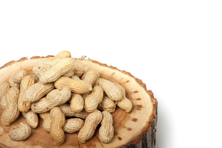 Pile of unshelled peanuts on wood slice, isolated on white backgroundの写真素材