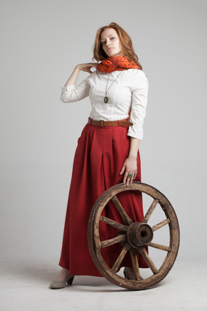 Young woman in long red skirt standing near the wheel of the cartの写真素材