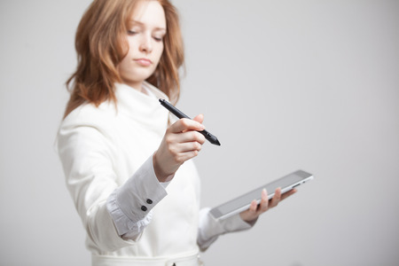 young woman with pen and tablet writes or shows on grey backgroundの写真素材