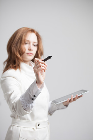 young woman with pen and tablet writes or shows on grey backgroundの写真素材