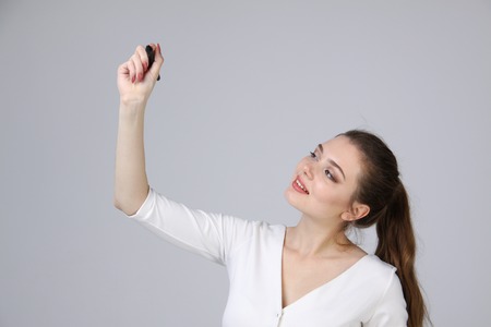young woman in white dress with pen  writes or shows on grey backgroundの写真素材