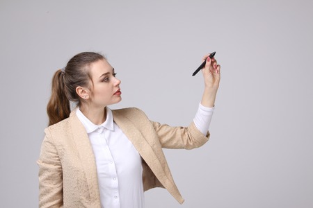 young woman with pen  writes or shows on grey backgroundの写真素材