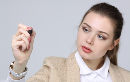 young woman with pen  writes or shows on grey backgroundの写真素材