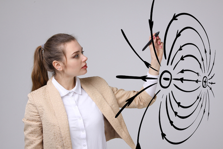 Young woman, physics teacher draws a diagram of the electric field, on gray backgroundの写真素材
