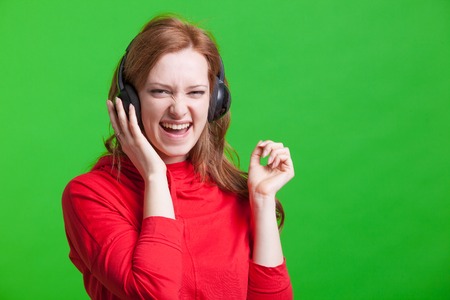 Young woman listening music on headphones on green backgroundの写真素材