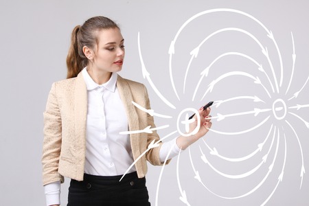 Young woman, physics teacher draws a diagram of the electric field, on gray backgroundの写真素材
