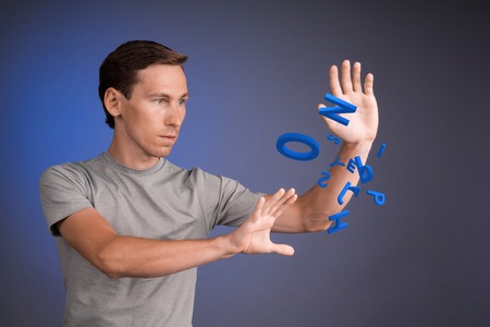 Young man in t-shirt working with a set of letters on blue background, writing concept.の写真素材