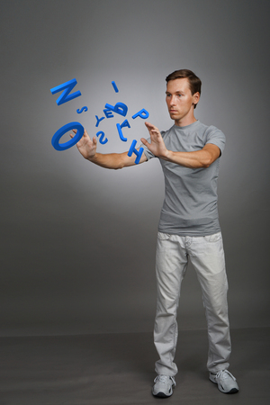 Young man in t-shirt working with a set of letters on grey background, writing concept.の写真素材