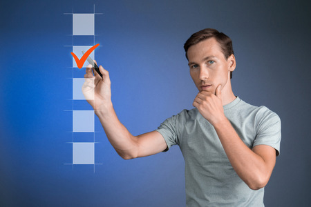 Young man t-shirt checking on checklist box. Blue background. Concept on the topic of elections.の写真素材