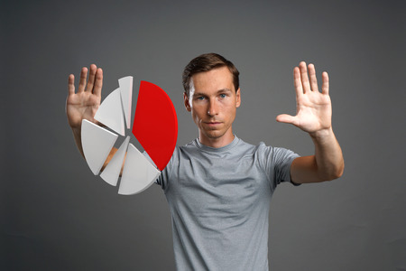 Young man in t-shirt working with pie chart on grey background. Concept on the topic of statistics or financial report.の写真素材