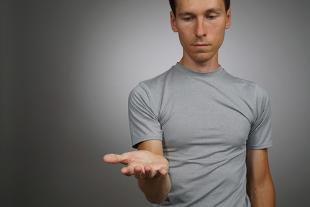 Young man in t-shirt holding something on his palmの写真素材