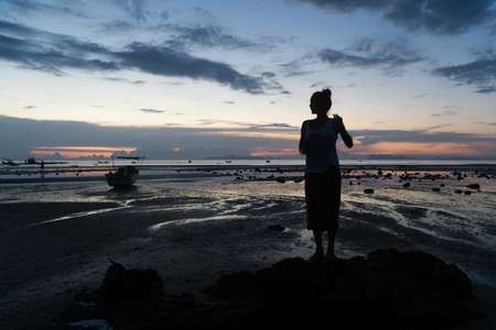 Female silhouette at sunset, woman stands on the sea beach.の写真素材