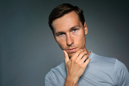 Thoughtful young man on gray background.の写真素材