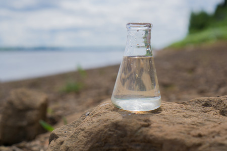 Chemical flask with water, lake or river in the background.の写真素材