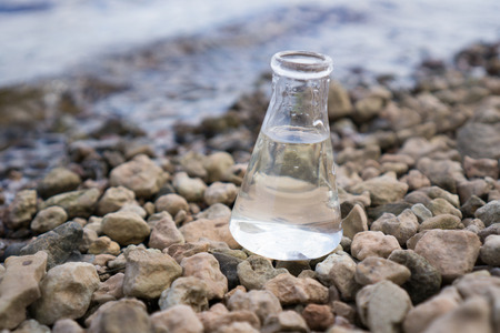 Chemical flask with water, lake or river in the background.の写真素材