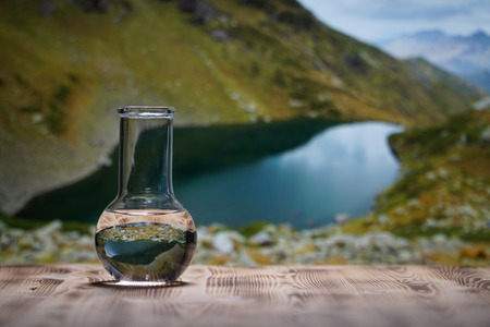 Clean water in a glass laboratory flask on wooden table on mountain background. Ecological concept, the test of purity and quality of water.の写真素材