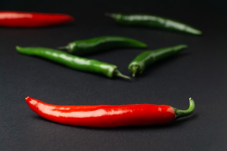 Green and red chili peppers on black background. Hot spicy food.