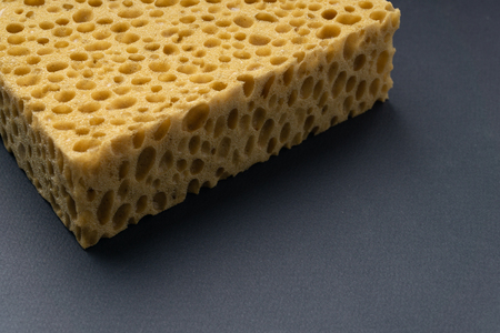 Close up view of cleaning sponge, mesh structure pattern on black surface. Yellow sponge close-up.の写真素材