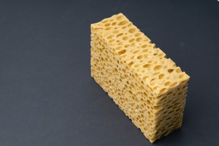 Close up view of cleaning sponge, mesh structure pattern on black surface. Yellow sponge close-up.の写真素材