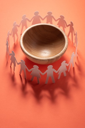 Circle of paper people holding hands in front of big empty bowl. Overpopulation, famine concept.