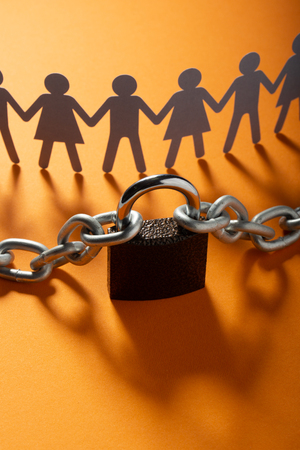 Human paper figures in front of metal chain and padlock on a orange surface. Freedom, human rights, independence.の写真素材