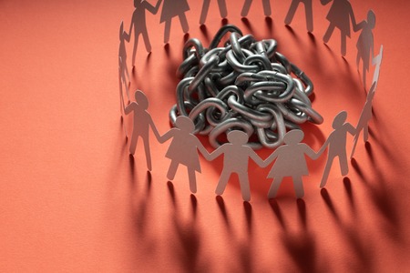 Human paper figures standing around a ball of metal chain on a red surface. Freedom, human rights, independence.の写真素材