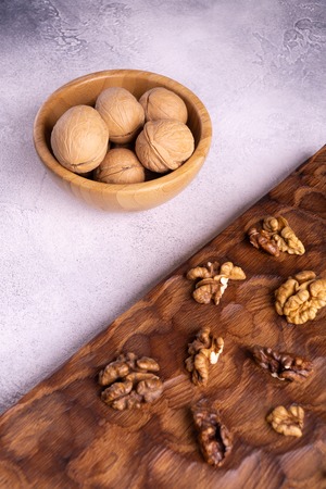 Walnuts in wooden bowl and on wooden carved board on bright textured surface. Healthy nuts and seeds...