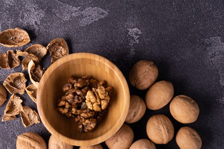 Walnuts in wooden bowl and on black slate surface. Healthy nuts and seeds composition.