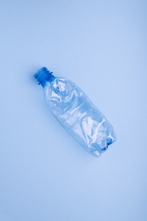 Crashed plastic bottle on bright blue background. Plastic utilisation concept. Ecological problem,...