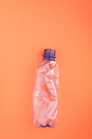 Crashed plastic bottle on orange background. Plastic utilisation concept. Ecological problem, global environment.の写真素材