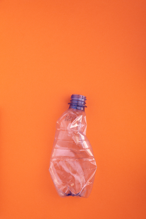 Crashed plastic bottle on orange background. Plastic utilisation concept. Ecological problem, global environment.の写真素材